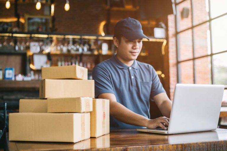 Homem mexendo em um notebook com varias caixas ao lado.