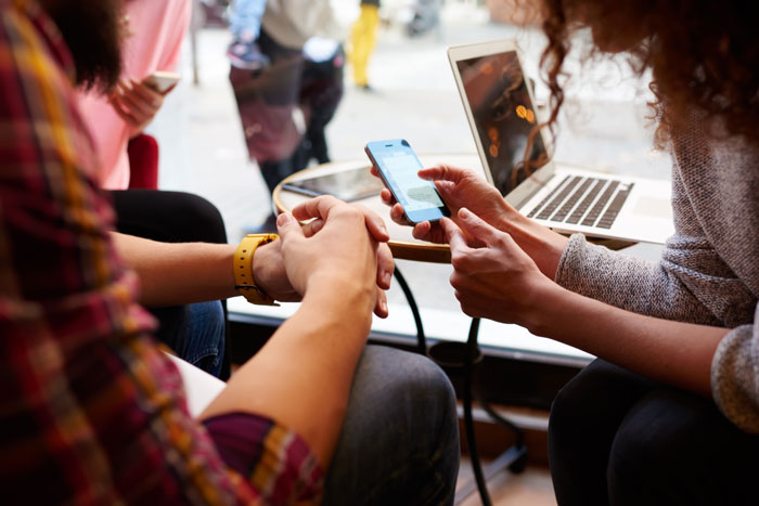 Mulher está fazendo uma compra on-line via telefone celular, enquanto está sentado com os amigos