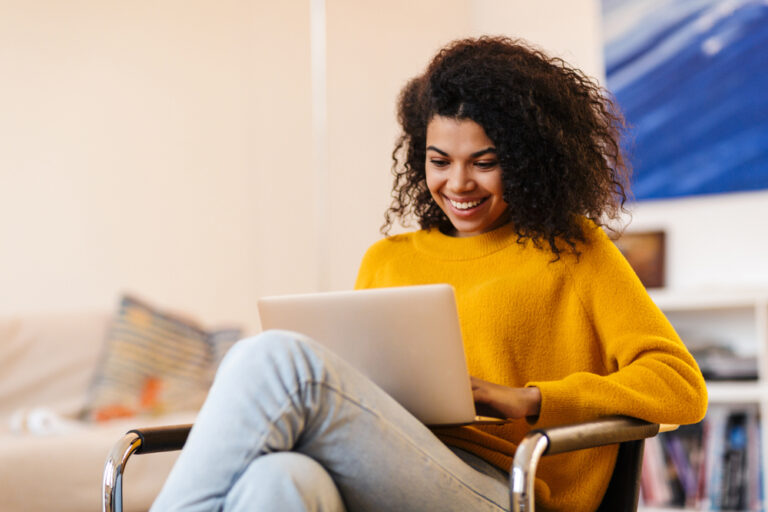 Mulher com blusa amarela, segurando computador e sorrindo