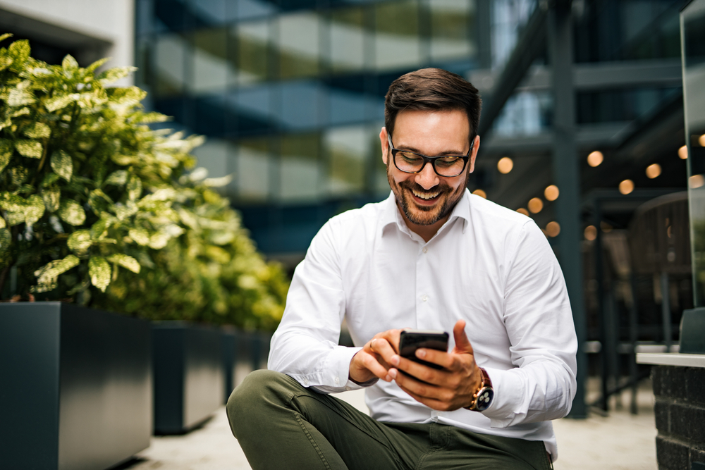 Homem mexendo no celular e sorrindo.