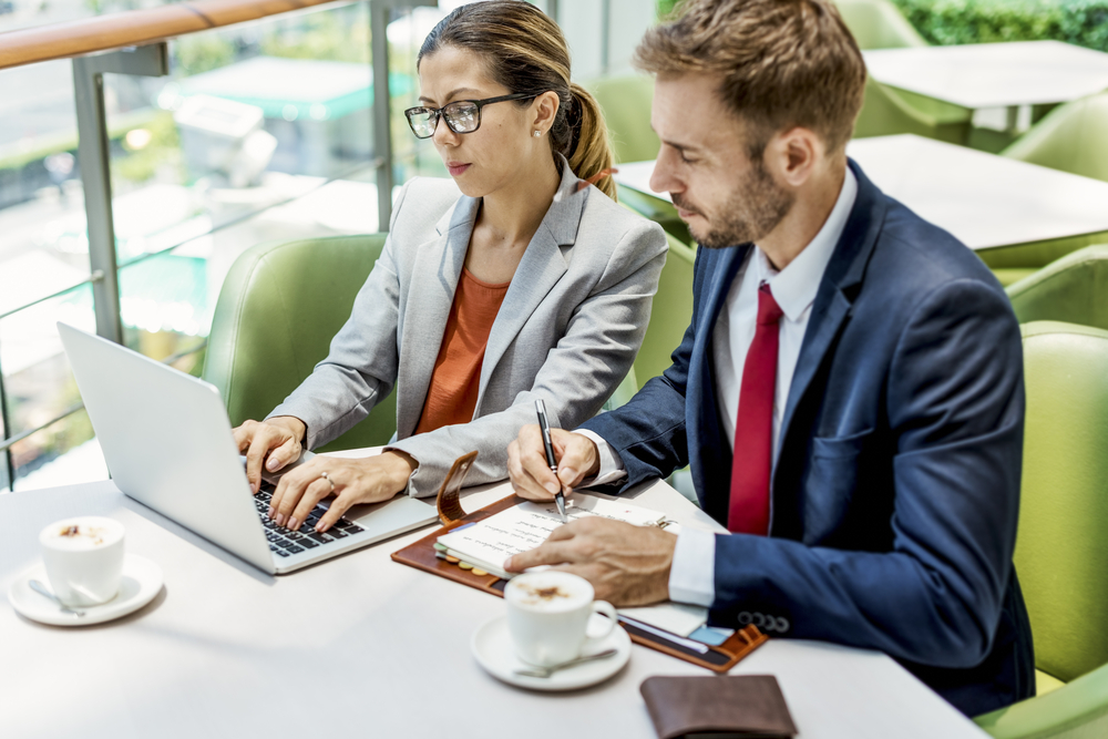 Uma mulher e um homem, sentados, olhando para um notebook