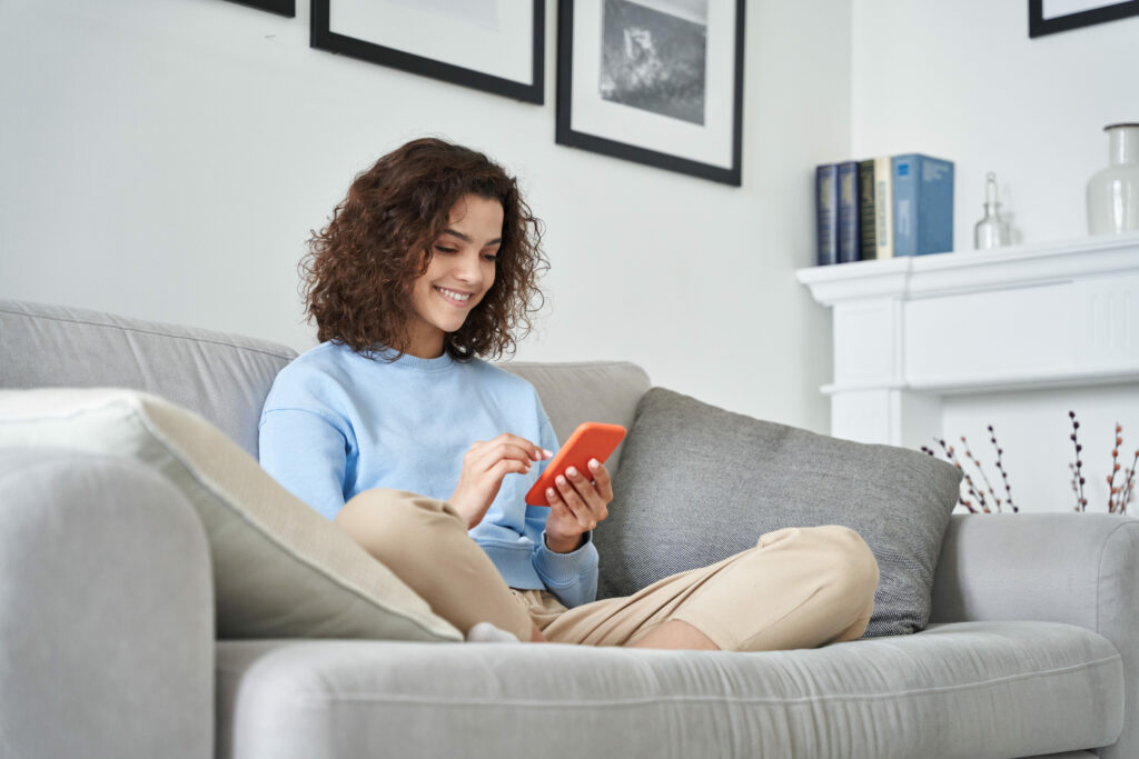 Feliz garota adolescente hispânica segurando telefone celular usando dispositivo smartphone em casa.